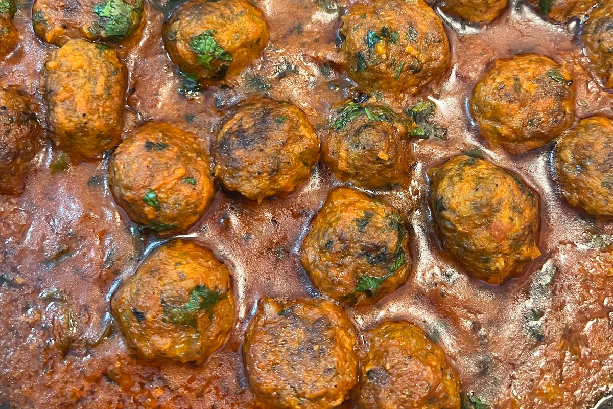 Panela com almôndegas douradas cozinhando em molho de tomate com salsinha por cima
