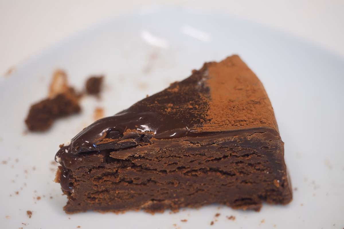 Fatia de bolo de chocolate escuro com cobertura brilhante em prato branco