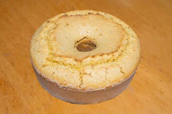 Fatia de bolo de fubá amarelo com casquinha dourada de queijo sobre prato branco