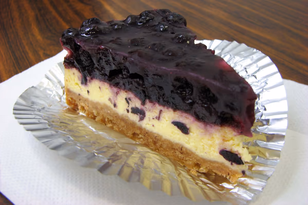 Fatia de cheesecake com base de biscoito e cobertura de calda de frutas vermelhas num prato