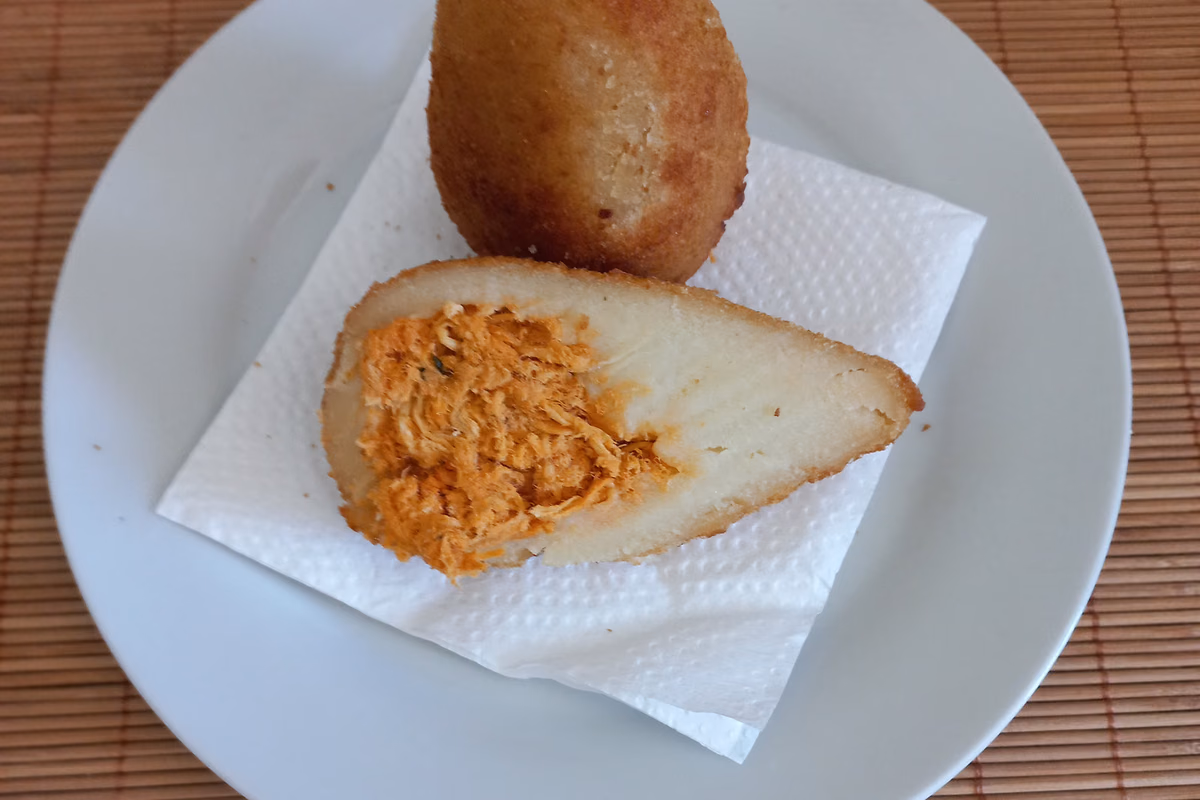 Coxinha de frango partida ao meio em prato branco, mostrando o recheio de frango desfiado