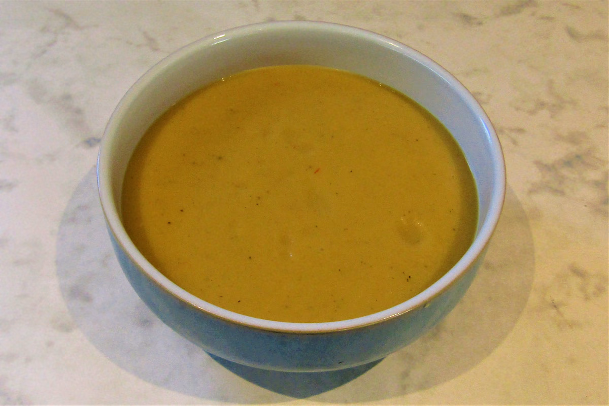 Tigela funda com creme de abóbora alaranjado e liso, com sementes por cima
