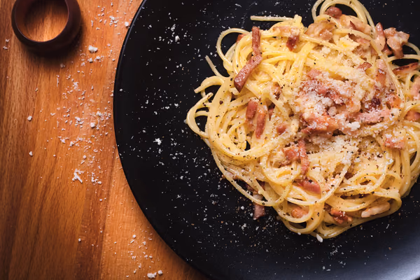 Prato de espaguete à carbonara cremoso com pedaços de bacon e pimenta moída por cima