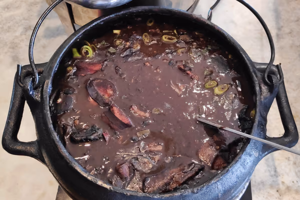Panela de ferro cheia de feijoada escura com pedaços de carne e linguiça na superfície