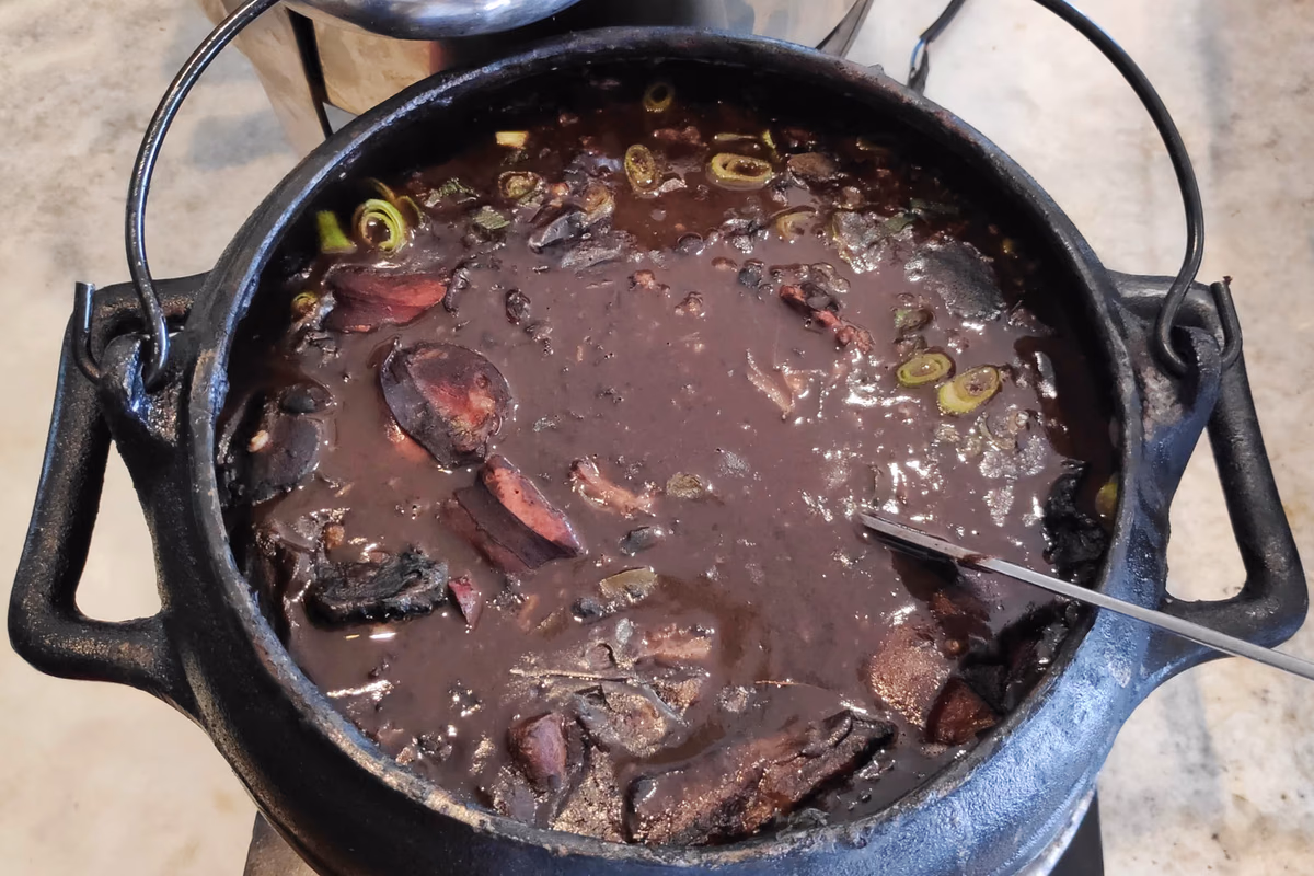 Panela de ferro cheia de feijoada escura com pedaços de carne e linguiça na superfície
