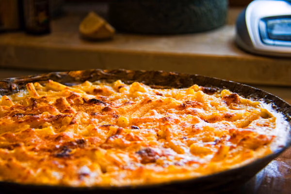 Macarrão gratinado com queijo derretido e crosta dourada numa frigideira de ferro
