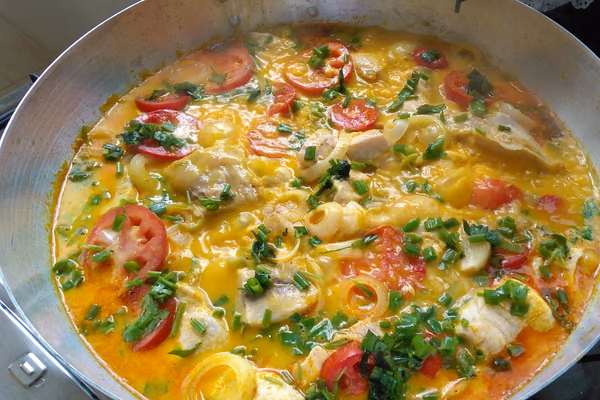 Panela larga com moqueca de peixe, rodelas de tomate, cebola e coentro picado por cima