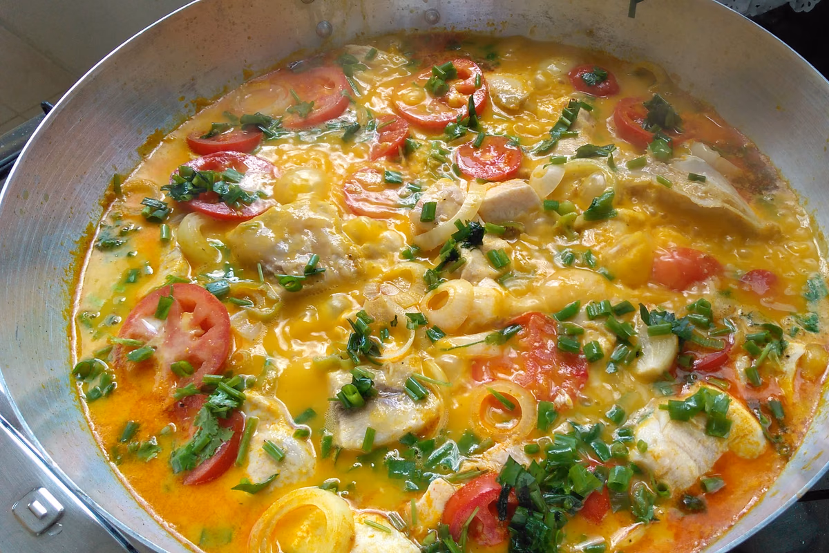 Panela larga com moqueca de peixe, rodelas de tomate, cebola e coentro picado por cima