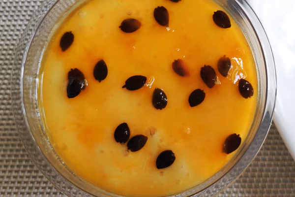 Taça de mousse de maracujá amarelo claro com calda de sementes por cima