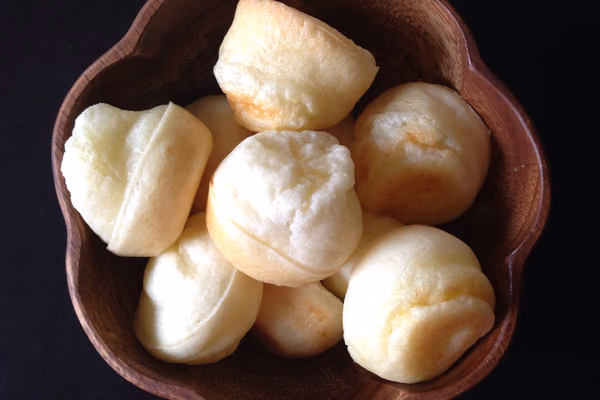 Tigela de madeira cheia de pães de queijo redondos e dourados, vistos de cima