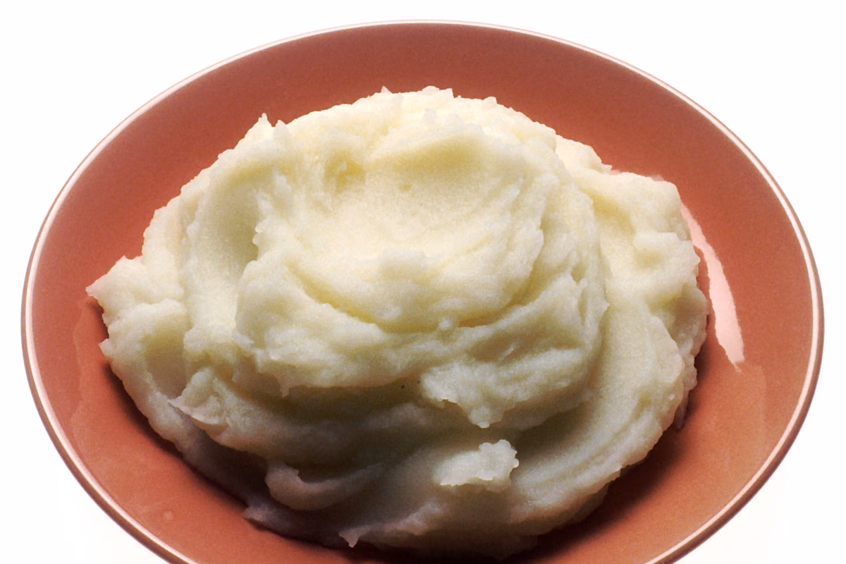 Tigela de purê de batata cremoso e claro, com manteiga derretendo no centro