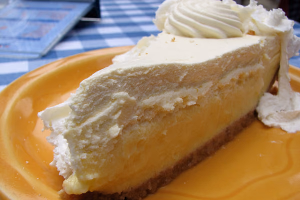 Fatia de torta de limão com base de biscoito e cobertura branca de merengue num prato